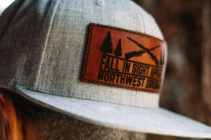 Guy wearing a gray fis hat with a leather patch with two shotguns and trees
